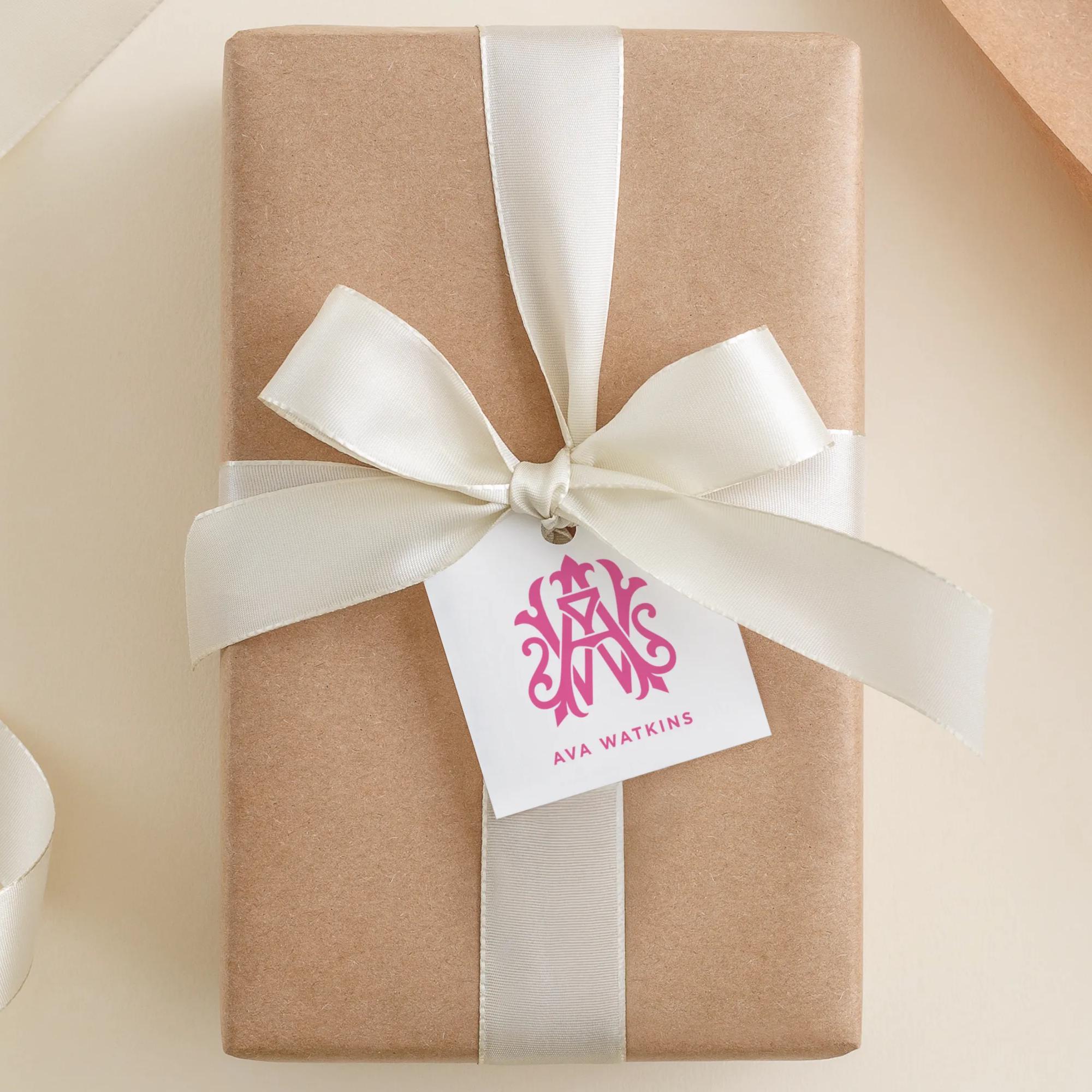 A brown gift box with a white ribbon and a pink monogrammed tag that reads "AVA WATKINS".